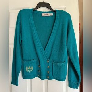 Cardigan style sweater with pockets, gold buttons and gold emblem.